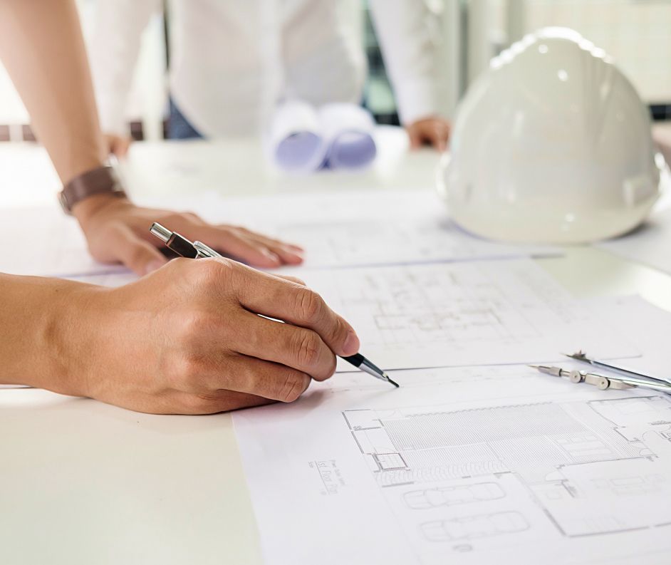 Zwei Hände die auf einem hellen Tisch auf eine Bauzeichnung schreiben