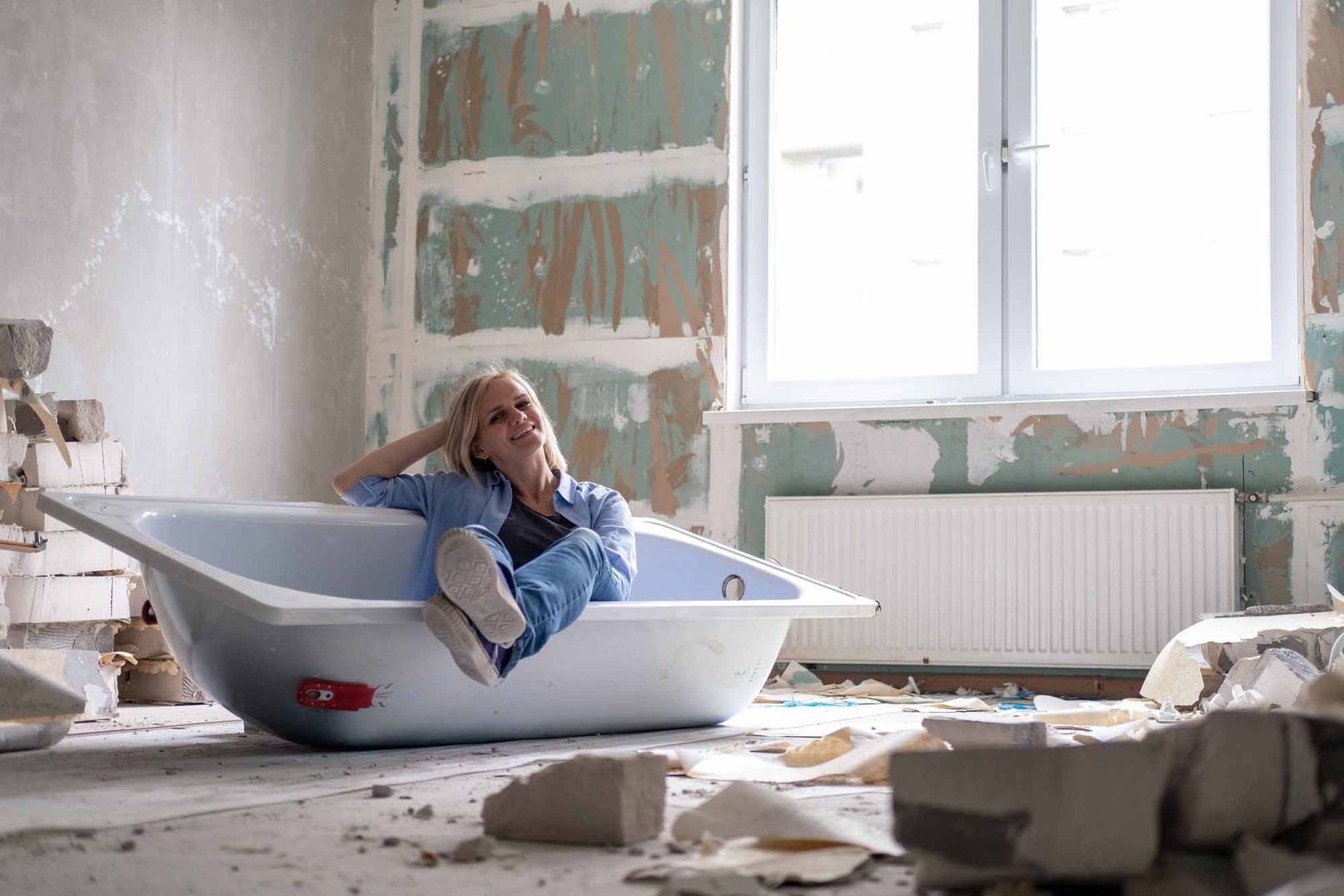 Frau sitzt in einer Badewanne in einem runtergerissenen Zimmer